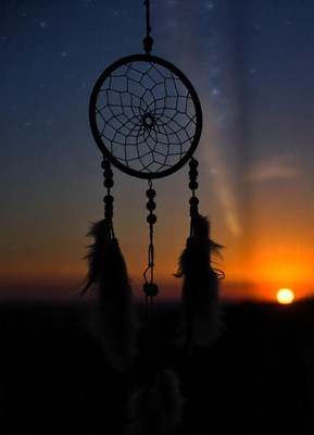 A dreamcatcher hangs against the setting sun