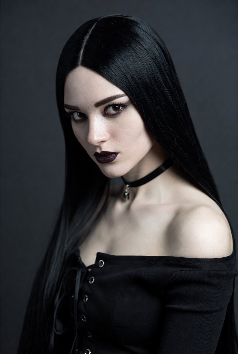 A woman with long black hair and bold makeup gazes intensely A woman with long black hair and bold makeup gazes intensely