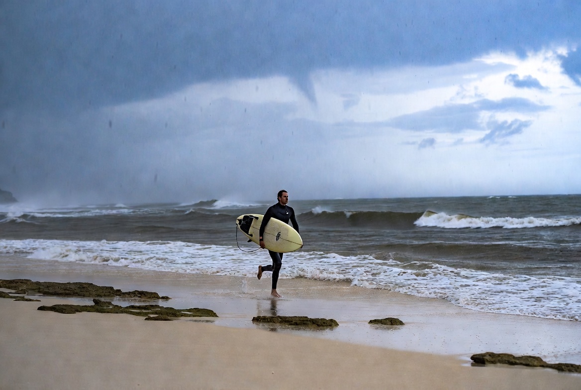 Surfer walks on beach during storm Surfer walks on beach during storm