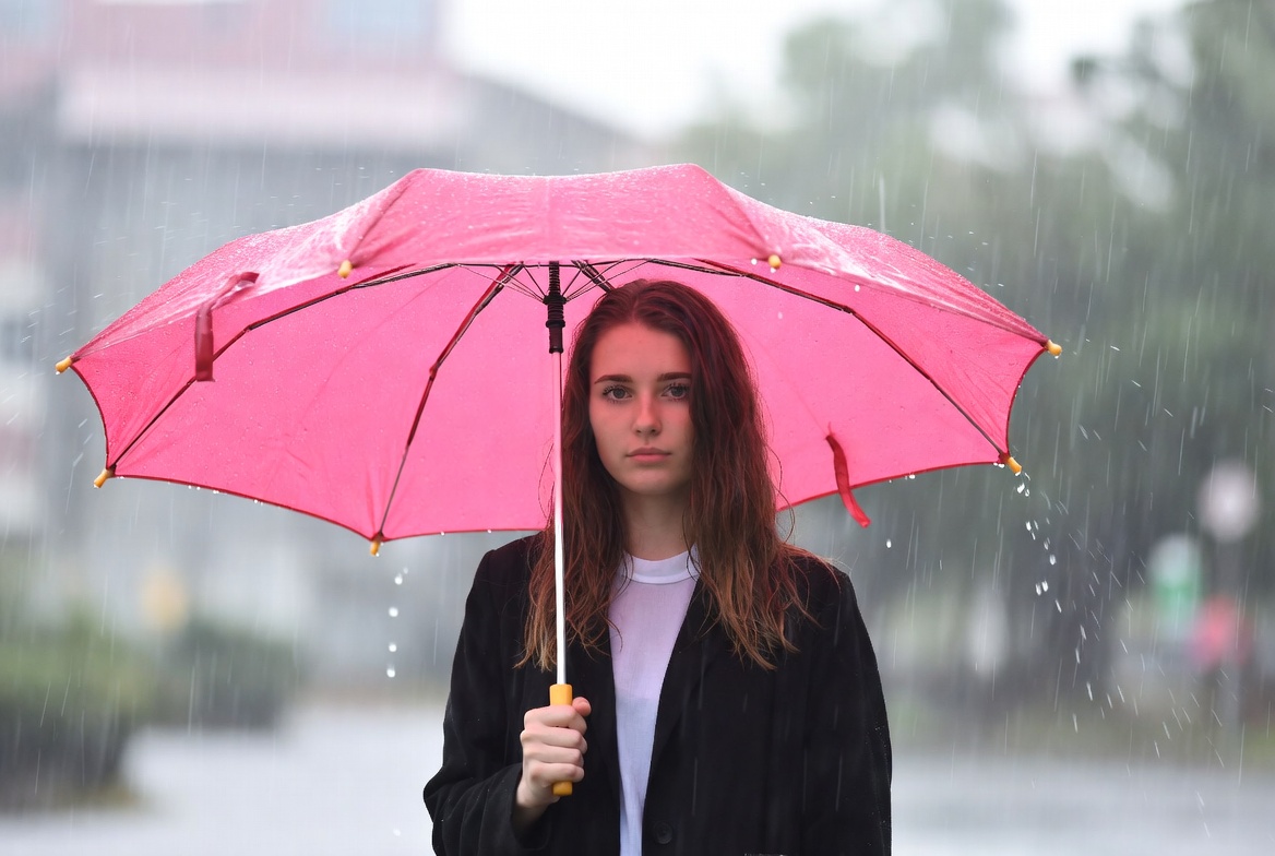 Girl standing under pink umbrella in rain Girl standing under pink umbrella in rain