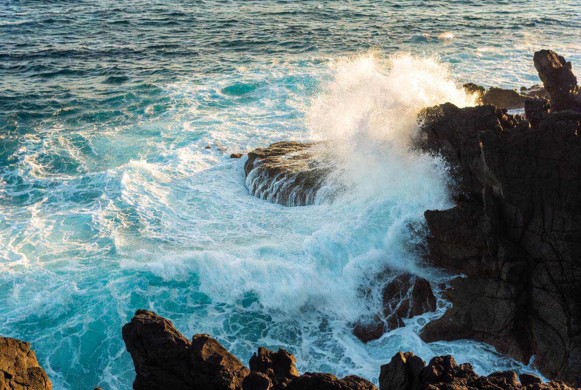 Waves crash on rocky shoreline in sunlight Waves crash on rocky shoreline in sunlight
