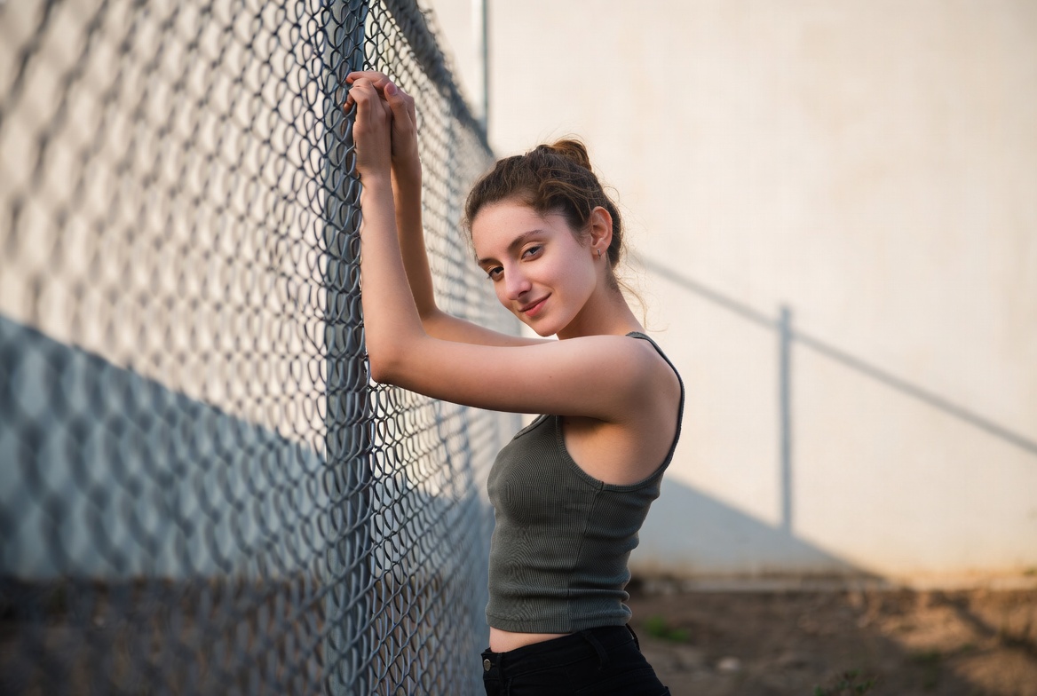 Young woman poses by fence at sunset Young woman poses by fence at sunset