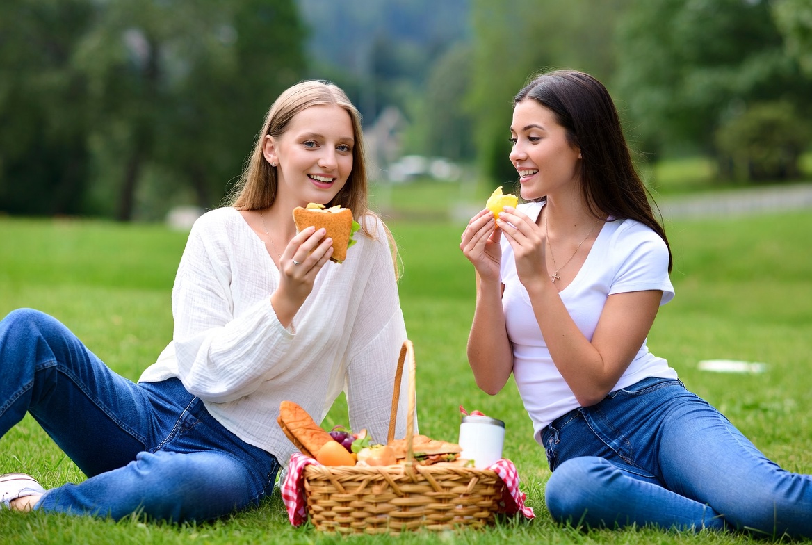 Two women eating sandwiches picnic outdoors Two women eating sandwiches picnic outdoors
