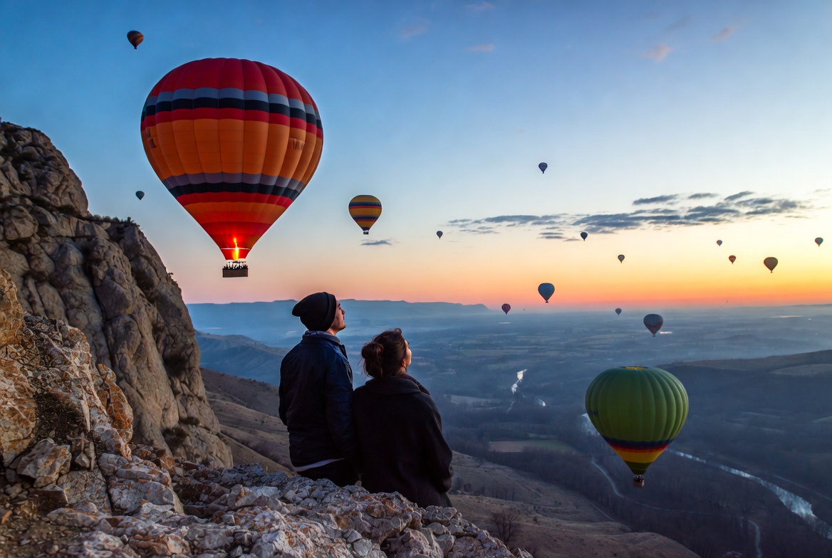 Couple watching hot air balloons from cliff Couple watching hot air balloons from cliff