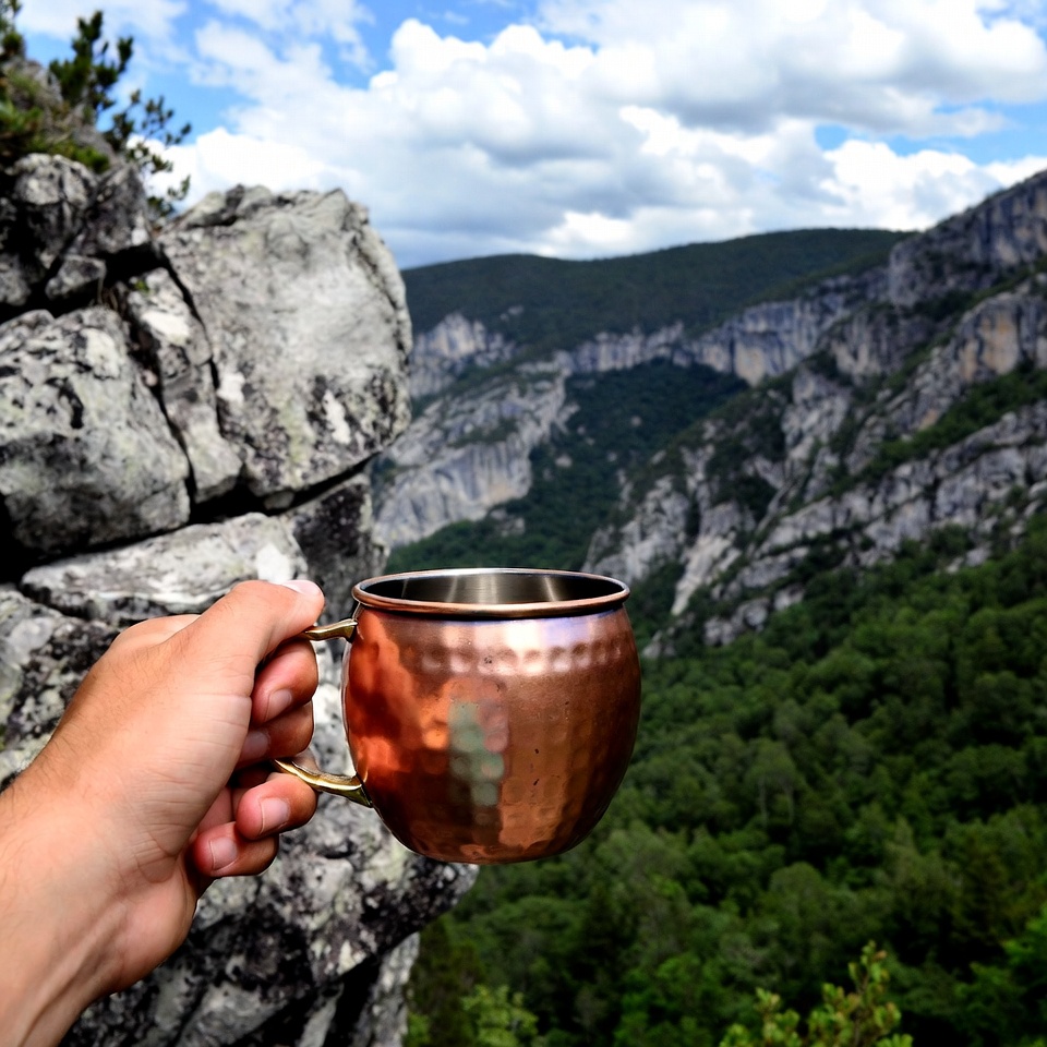 Hand holding copper mug over mountain cliff Hand holding copper mug over mountain cliff