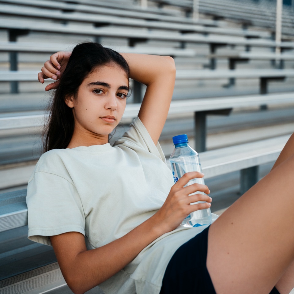 Teen girl holding water bottle on bleachers Teen girl holding water bottle on bleachers