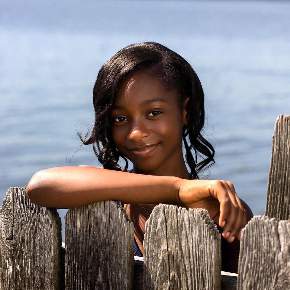 African-American girl leaning on wooden fence by lake African-American girl leaning on wooden fence by lake