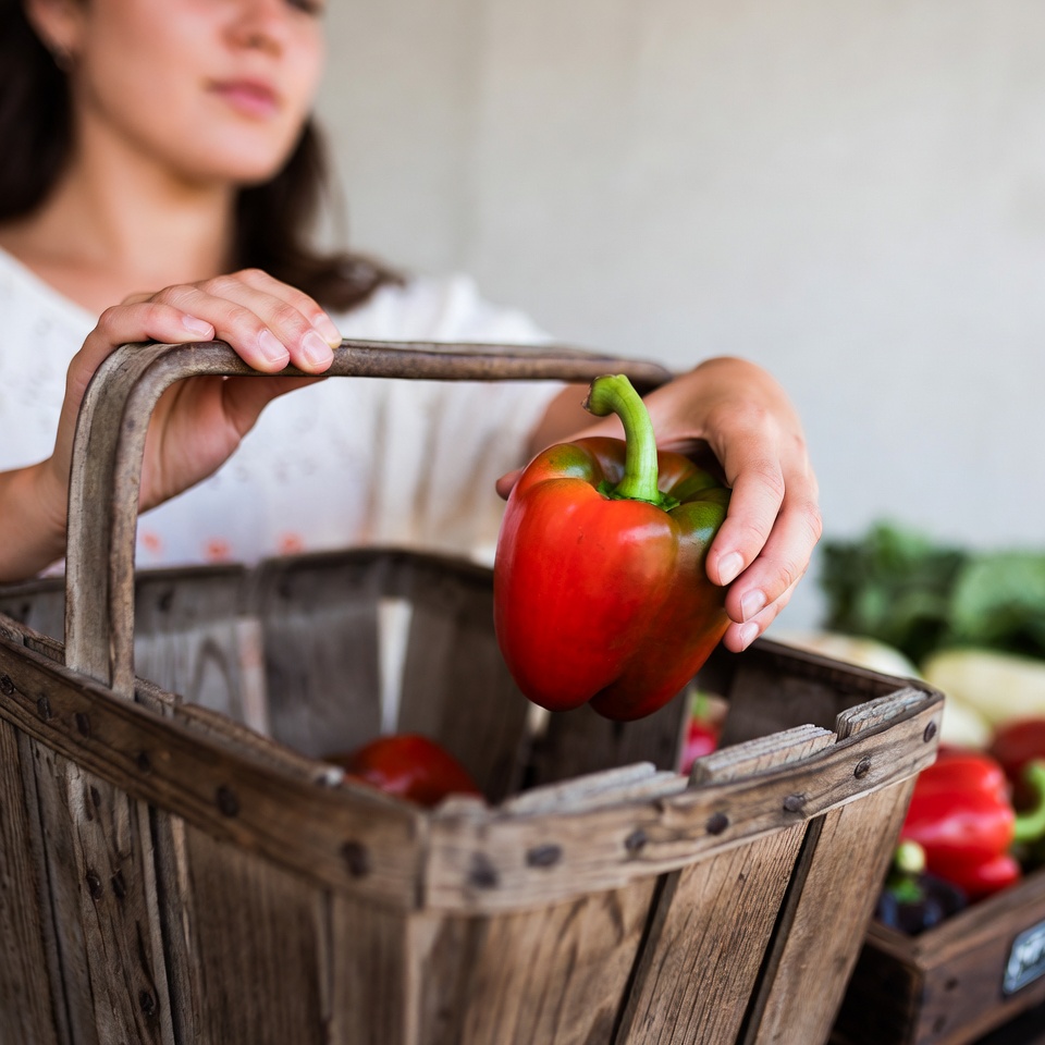 Woman holding red bell pepper in basket Woman holding red bell pepper in basket