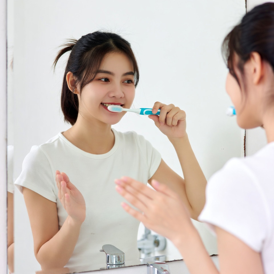 Asian woman brushing teeth in mirror Asian woman brushing teeth in mirror
