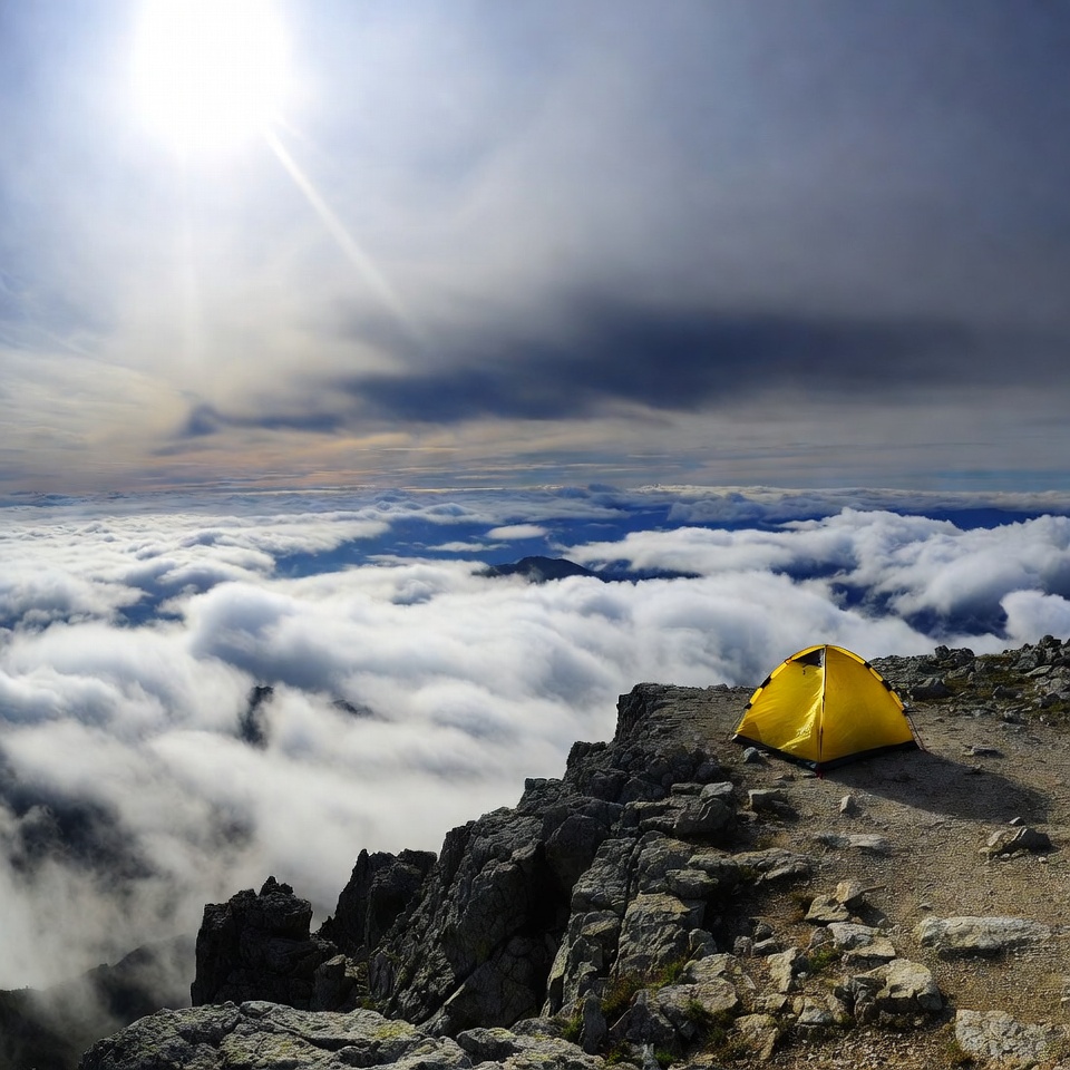 Yellow tent on mountain peak above clouds Yellow tent on mountain peak above clouds