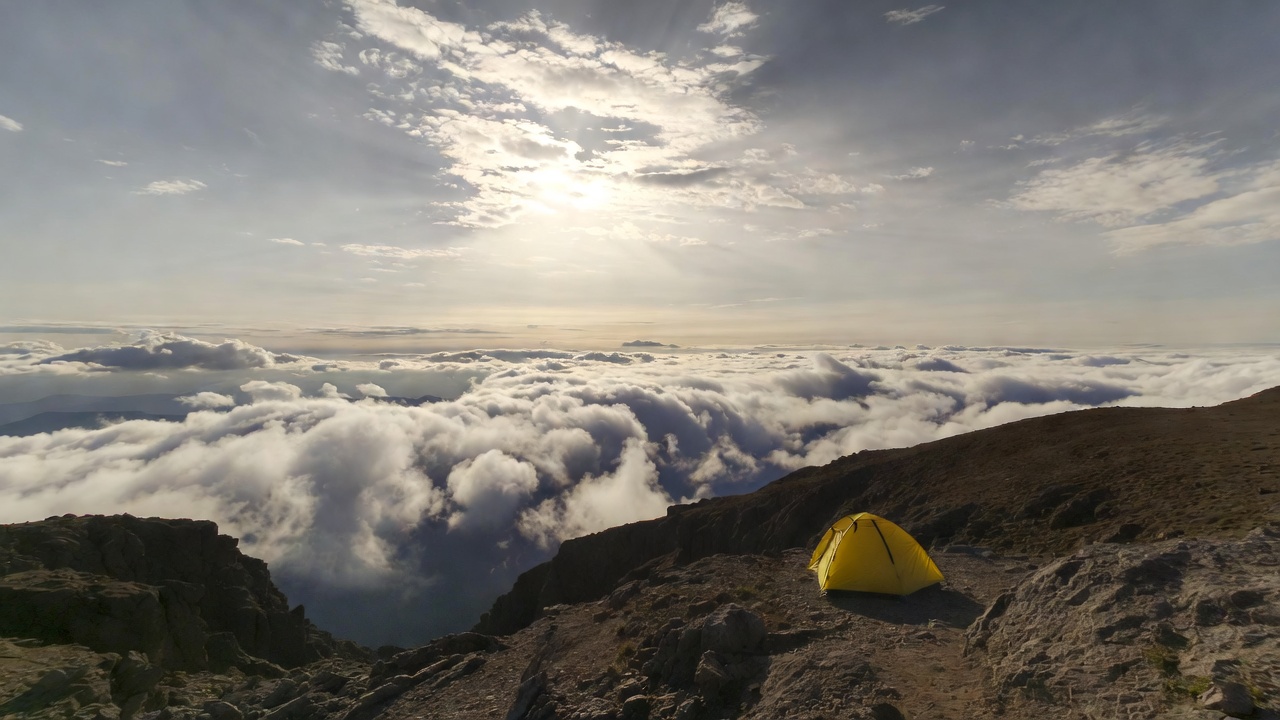 Yellow tent on mountain above clouds Yellow tent on mountain above clouds