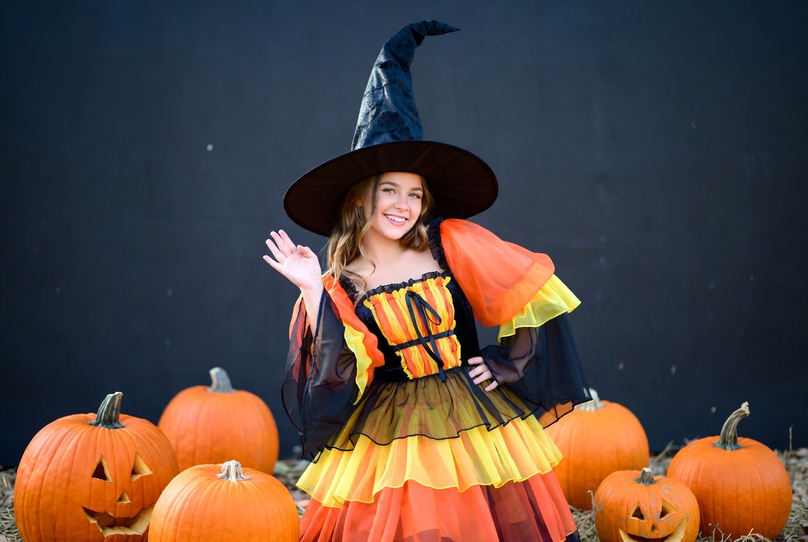Girl waving in witch costume with pumpkins Girl waving in witch costume with pumpkins