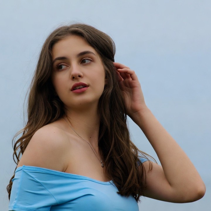 Woman touching ear in blue off-shoulder top Woman touching ear in blue off-shoulder top