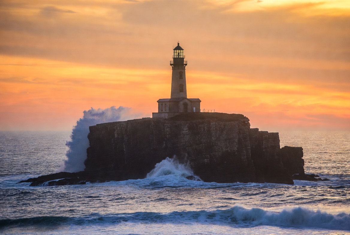 Lighthouse on rocky island at sunset Lighthouse on rocky island at sunset