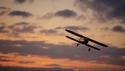 A biplane flies through a cloudy sunset