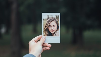 A hand holds a photo of a woman in the woods