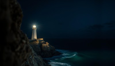 A lighthouse shines bright on a rocky cliff at night