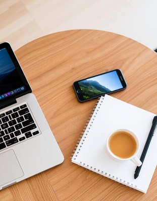 A laptop, smartphone, notepad, and coffee on a wooden table