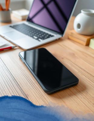 Smartphone on wooden desk, laptop behind it