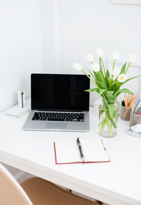 A laptop and notebook sit on a desk with tulips