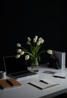 A white desk with a laptop, notebooks, and a vase of tulips