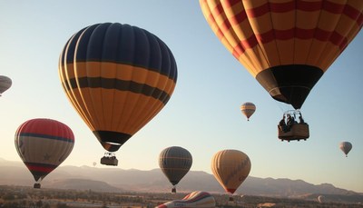 Hot air balloons soar over a mountain range at sunrise