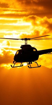 A helicopter flies in front of a golden sunset