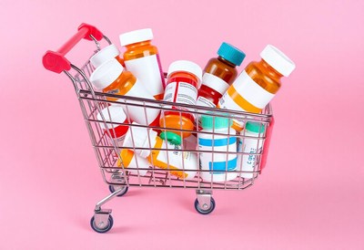 A shopping cart filled with pills on a pink background