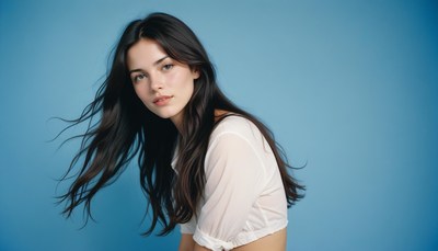 Woman with long dark hair poses by blue backdrop