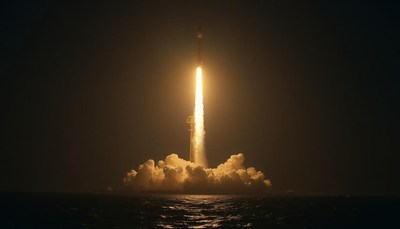 A rocket launches into the night sky over the ocean