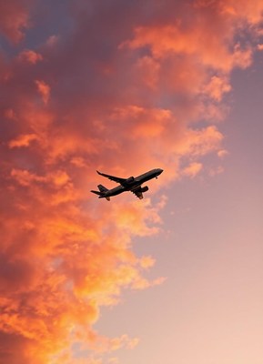 An airplane flies through a sunset sky
