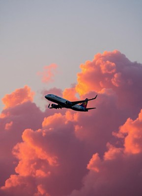 An airplane flies through pink clouds at sunset