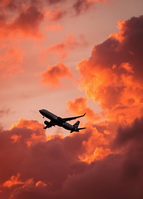 An airplane flies through a fiery sunset sky