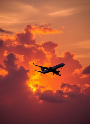 An airplane flies through a vibrant sunset