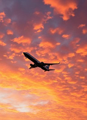 An airplane flies through a vibrant sunset sky
