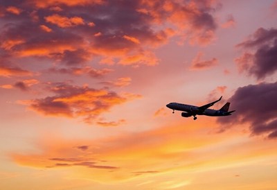 An airplane flies through a sunset sky