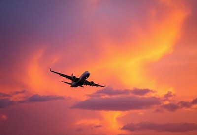 An airplane flies through a vibrant sunset sky