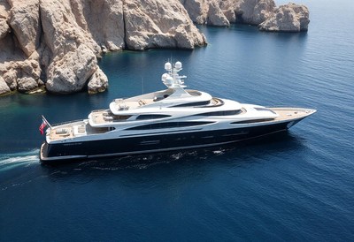 A large yacht sails through the open sea near rocky cliffs