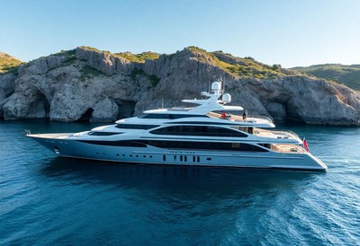 A large yacht sails past rocky cliffs on a sunny day