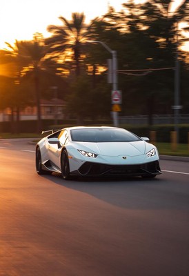 A white sports car drives down a street at sunset
