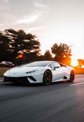 A white sports car drives down a road at sunset