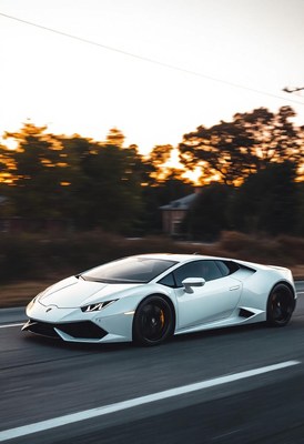 A white sports car drives down a road at sunset