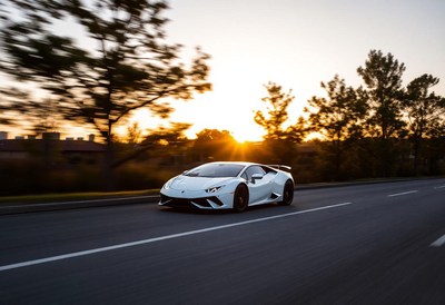 A white sports car drives down a road at sunset