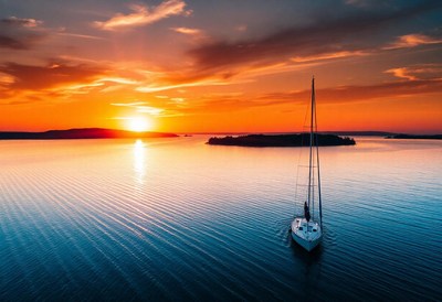 A sailboat glides through calm waters at sunset