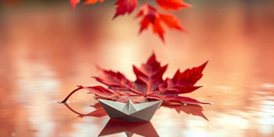 A paper boat floats on water with a red maple leaf beside it