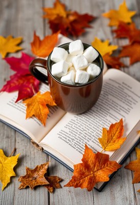 Hot cocoa with marshmallows on a book, autumn leaves