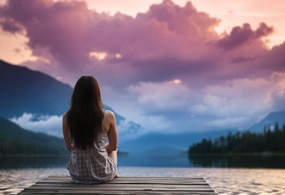 A woman sits on a dock overlooking a lake at sunset