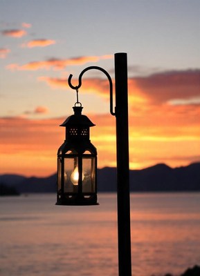 A lantern hangs against a sunset over the water
