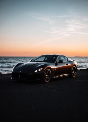 A black sports car parked by the ocean at sunset