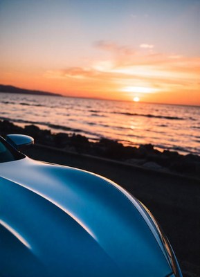 A blue car parked by the ocean at sunset
